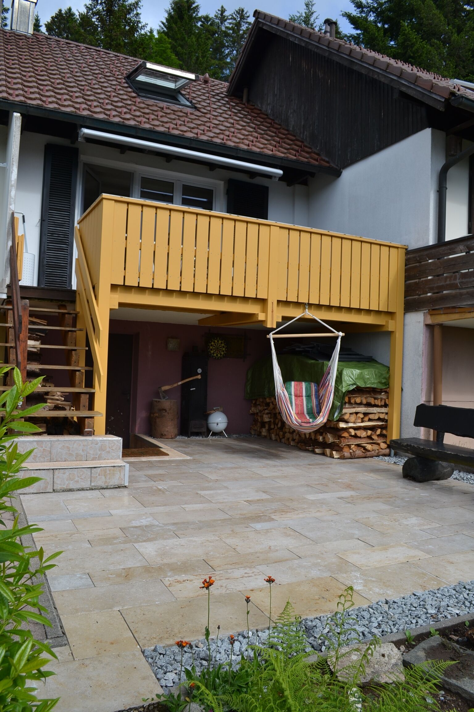 A house with a yellow balcony, a wooden staircase, and a hanging hammock.
