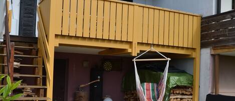 A house with a yellow balcony, a wooden staircase, and a hanging hammock.