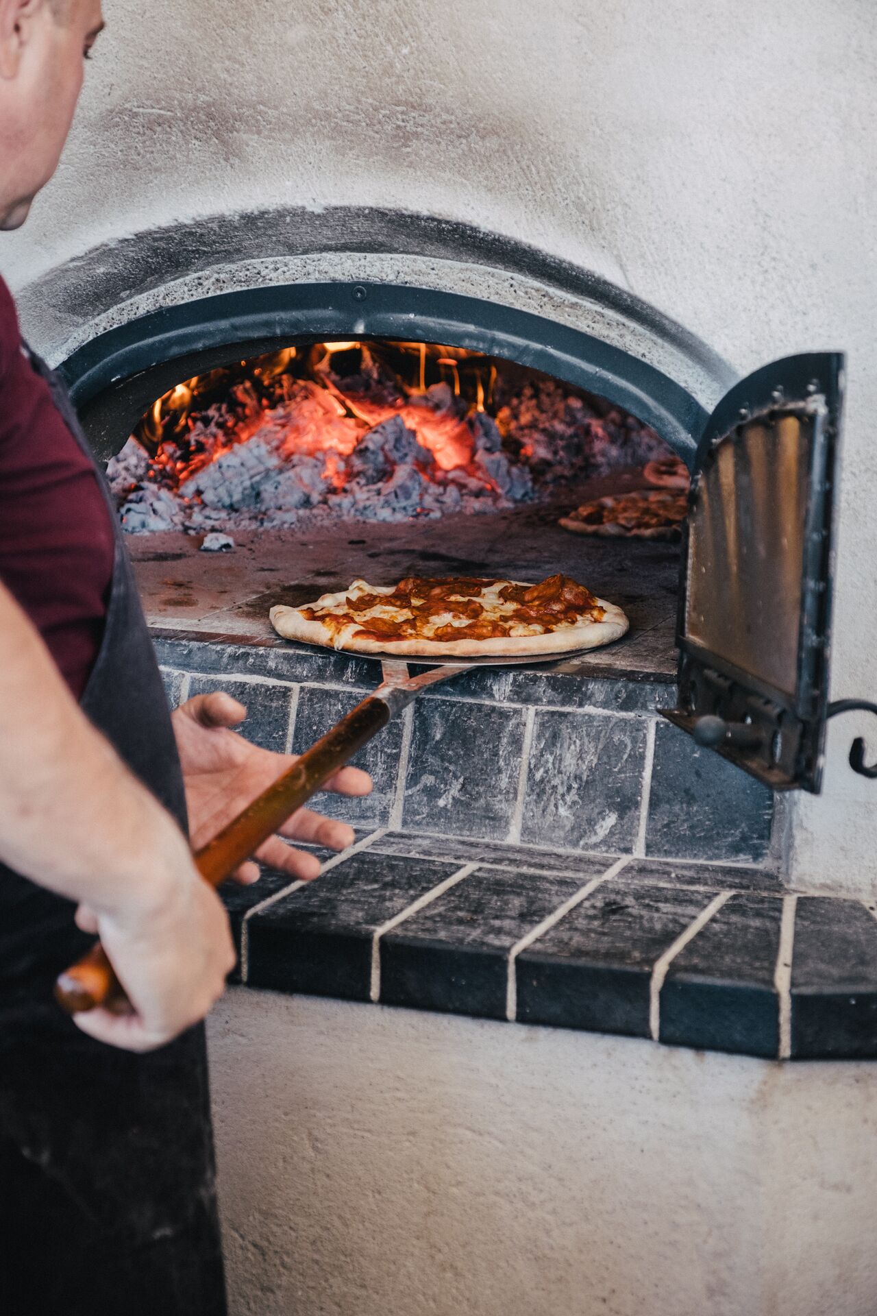 A person using a pizza peel to place a pizza into a brick oven.