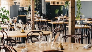 A restaurant with round tables, dark wooden chairs, and bamboo pendant lights. - Hotel Strana (Hälleviksstrand)