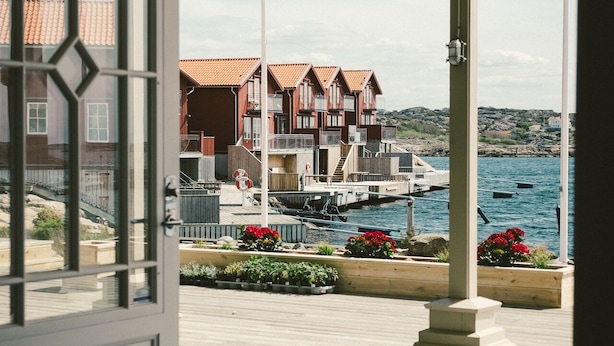 A wooden deck with a view of a coastal town, featuring buildings with red roofs and a marina. - Hotel Strana (Hälleviksstrand)