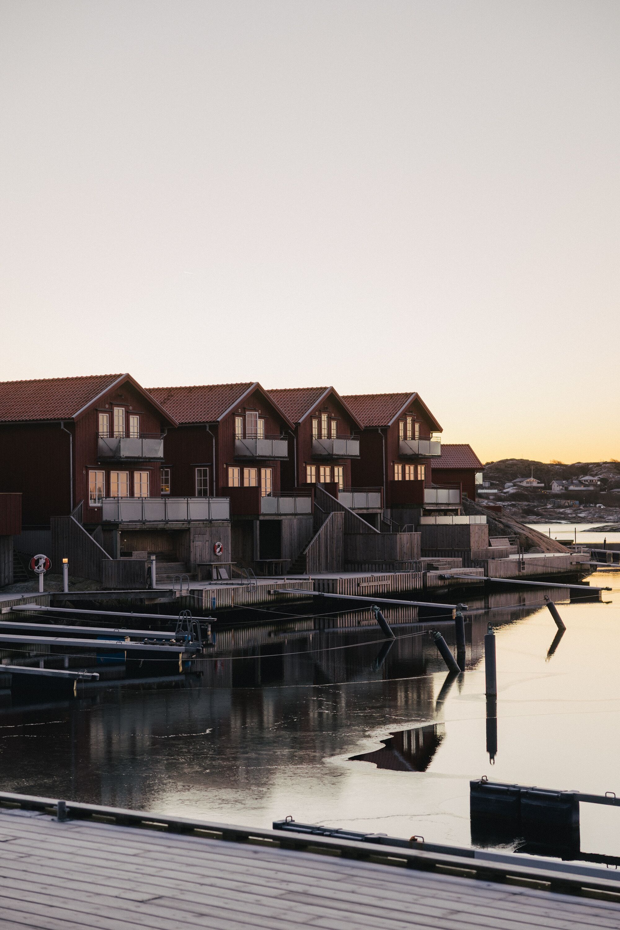 A waterfront building with multiple balconies, a wooden deck, and a calm water body reflecting the structure.