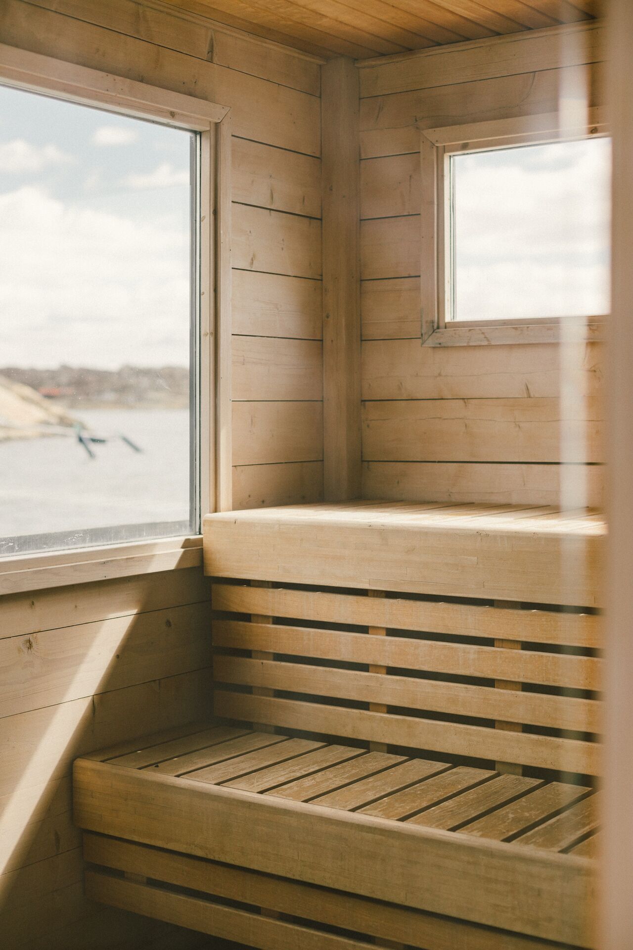 Una cabaña de madera con un banco y una ventana que da a un cuerpo de agua.