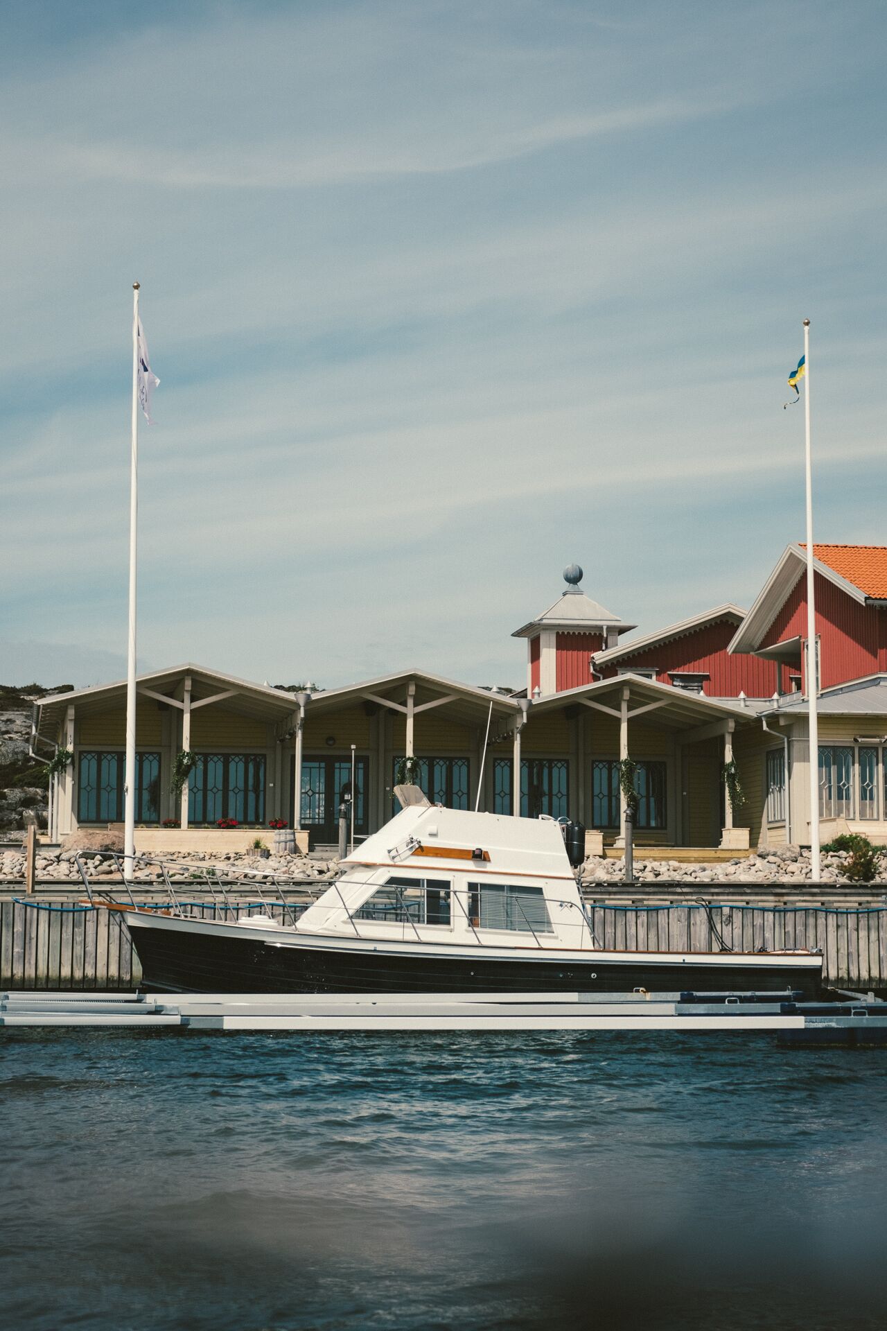 A marina with a docked boat, a building with multiple windows, and a flagpole with a flag.