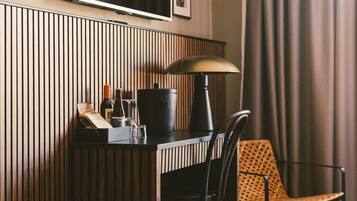 A hotel room with a wooden panel wall, a flat-screen TV mounted above a desk, a lamp, a chair, and a bed with a patterned cover.