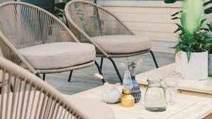 A cozy outdoor seating area with wicker chairs and a wooden table, featuring potted plants and decorative items. - Hotel Strana (Hälleviksstrand)