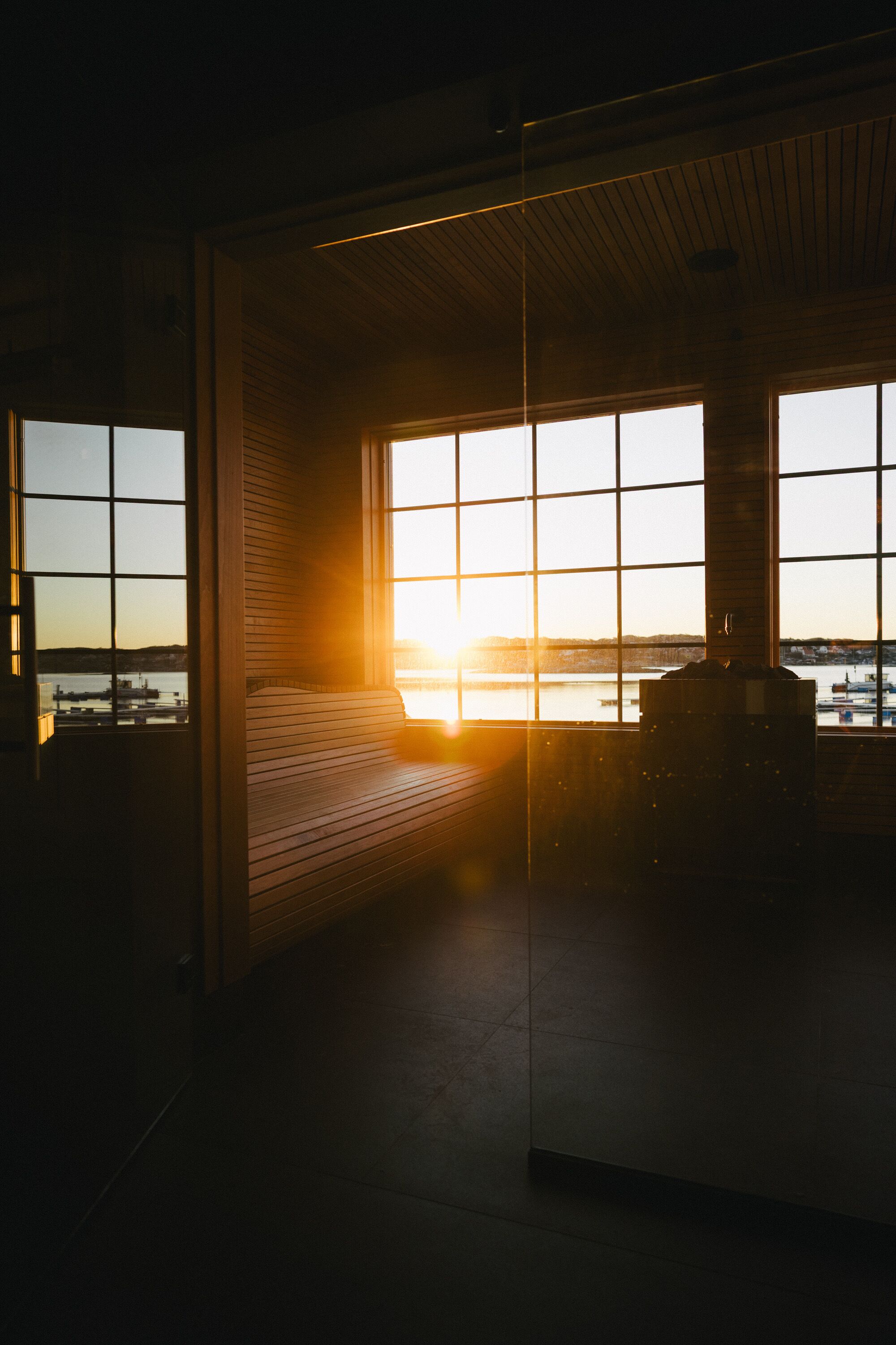 A room with large windows, a fireplace, and a view of a body of water during sunset.