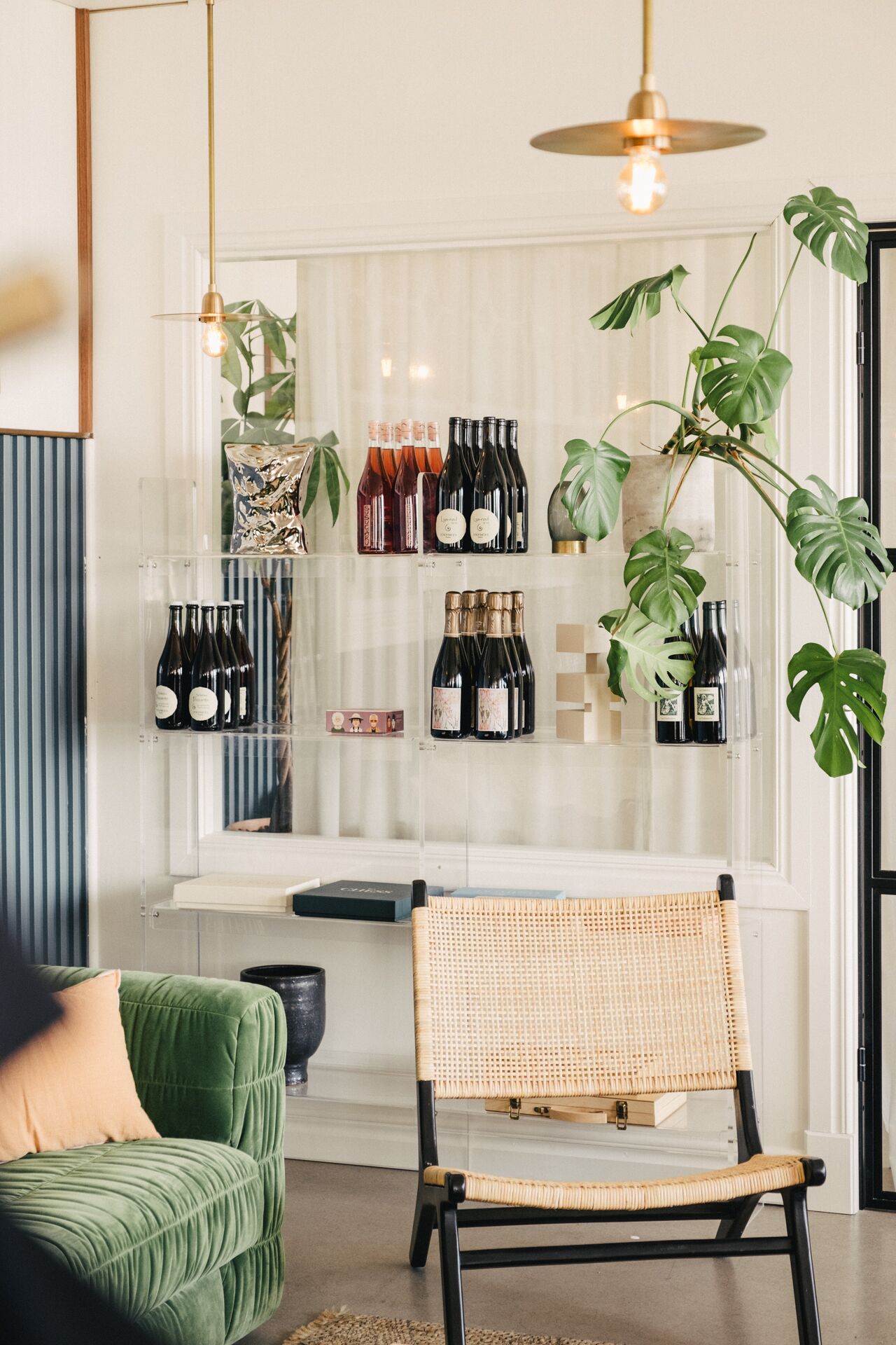 Une pièce avec un canapé vert, un fauteuil en osier et un meuble à bouteilles.