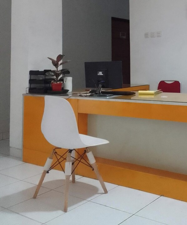 A reception desk with a white chair in front, a computer, and a small plant. - OYO 93808 Lincoln Dormitory (Curug)