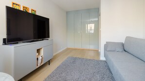 A modern living room with a flat-screen TV on a white cabinet, a grey sofa, and a glass wardrobe. - ShortStayPoland Aleja Stanów Zjednoczonych (B159) (Warsaw)