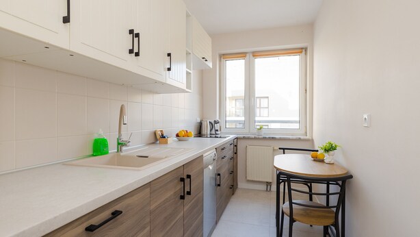 A modern kitchen with white cabinets, a wooden countertop, a sink, a kettle, and a dining table with chairs. - ShortStayPoland Aleja Stanów Zjednoczonych (B159) (Warsaw)