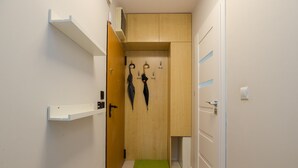 A narrow hallway with a wooden door, a green mat at the entrance, and a coat rack with two umbrellas. - ShortStayPoland Aleja Stanów Zjednoczonych (B159) (Warsaw)