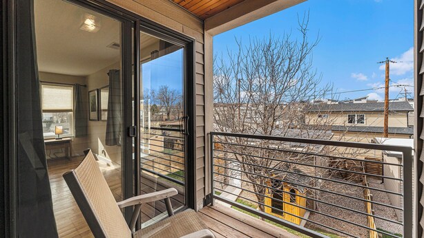 A balcony with a view of a tree and buildings, a chair, and a table with a lamp. - Spacious Denver Home with Hot tub and Rooftop (Denver)