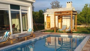 Ein Swimmingpool mit Liegestühlen, einer überdachten Sitzgelegenheit und Blick auf ein Haus mit großen Fenstern.