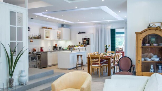 Eine moderne Küche mit weißen Schränken, ein Essbereich mit Holzkästen und ein Wohnzimmer mit einem weißen Sofa.