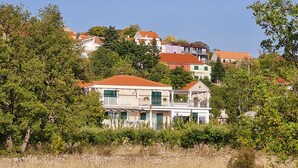 Eine Küstenvilla mit Balkon, umgeben von üppigem Grün und wolkenlosem Himmel.