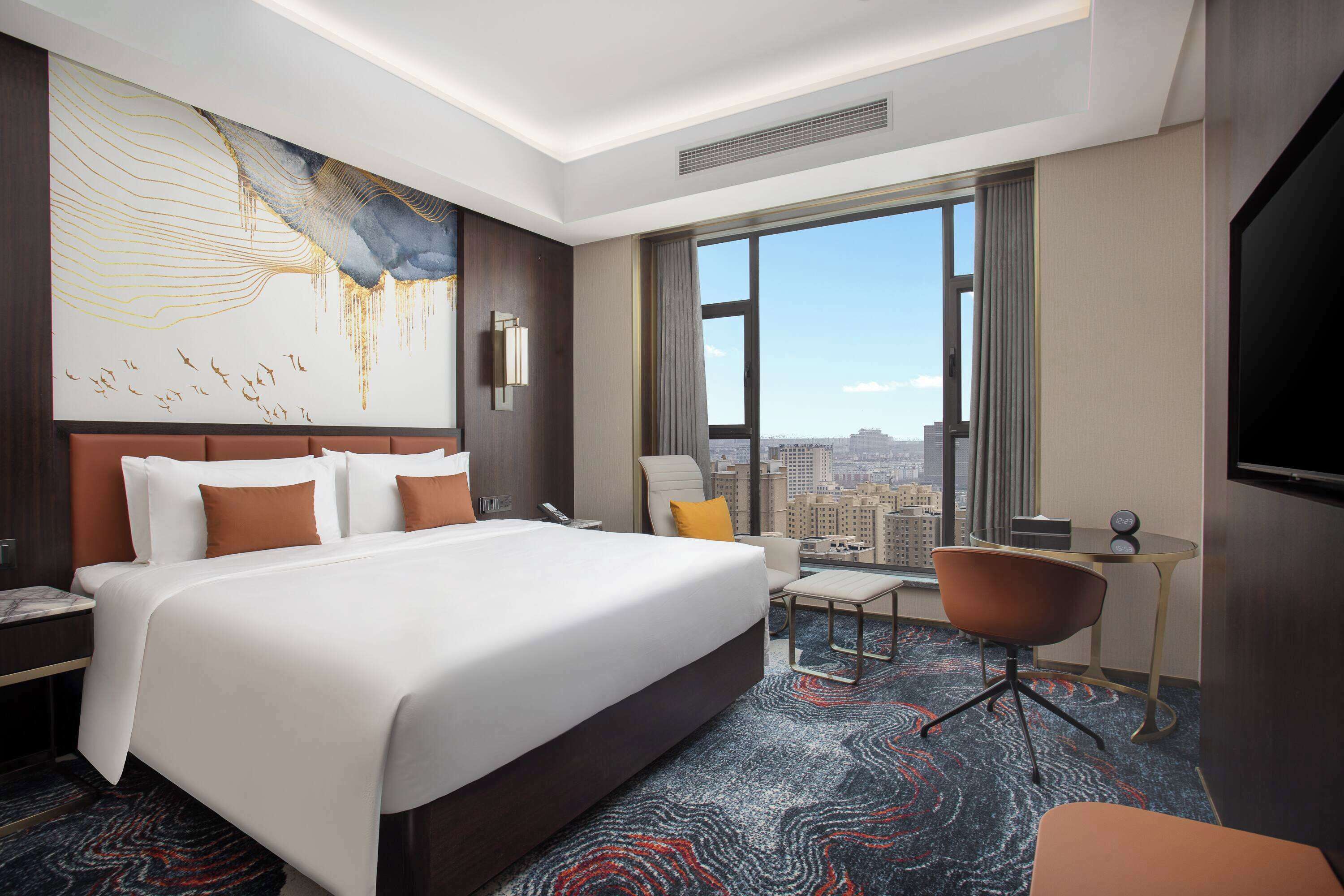 A hotel room with a large bed, a desk, a chair, and a view of the city.