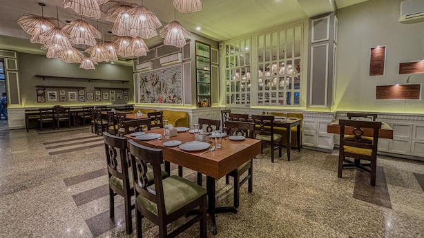A restaurant with multiple dining tables and chairs, large windows, and hanging pendant lights. - Hotel Bizzotel (Gurugram)