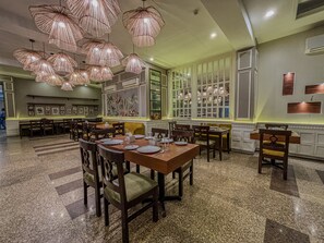 A restaurant with multiple dining tables and chairs, large windows, and hanging pendant lights. - Hotel Bizzotel (Gurugram)