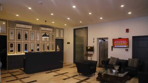 A lobby with a reception desk, seating area, and a television screen displaying a message. - Hotel Bizzotel (Gurugram)