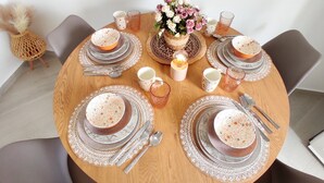 A round wooden dining table set for four with patterned tableware, a vase of flowers, and a candle centerpiece. - Modern Mykonos 2 Bd Aqua w shared Pool (Mykonos)