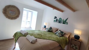 Une chambre à coucher avec un lit, une fenêtre, un miroir fixé au mur et une table de chevet avec une lampe.