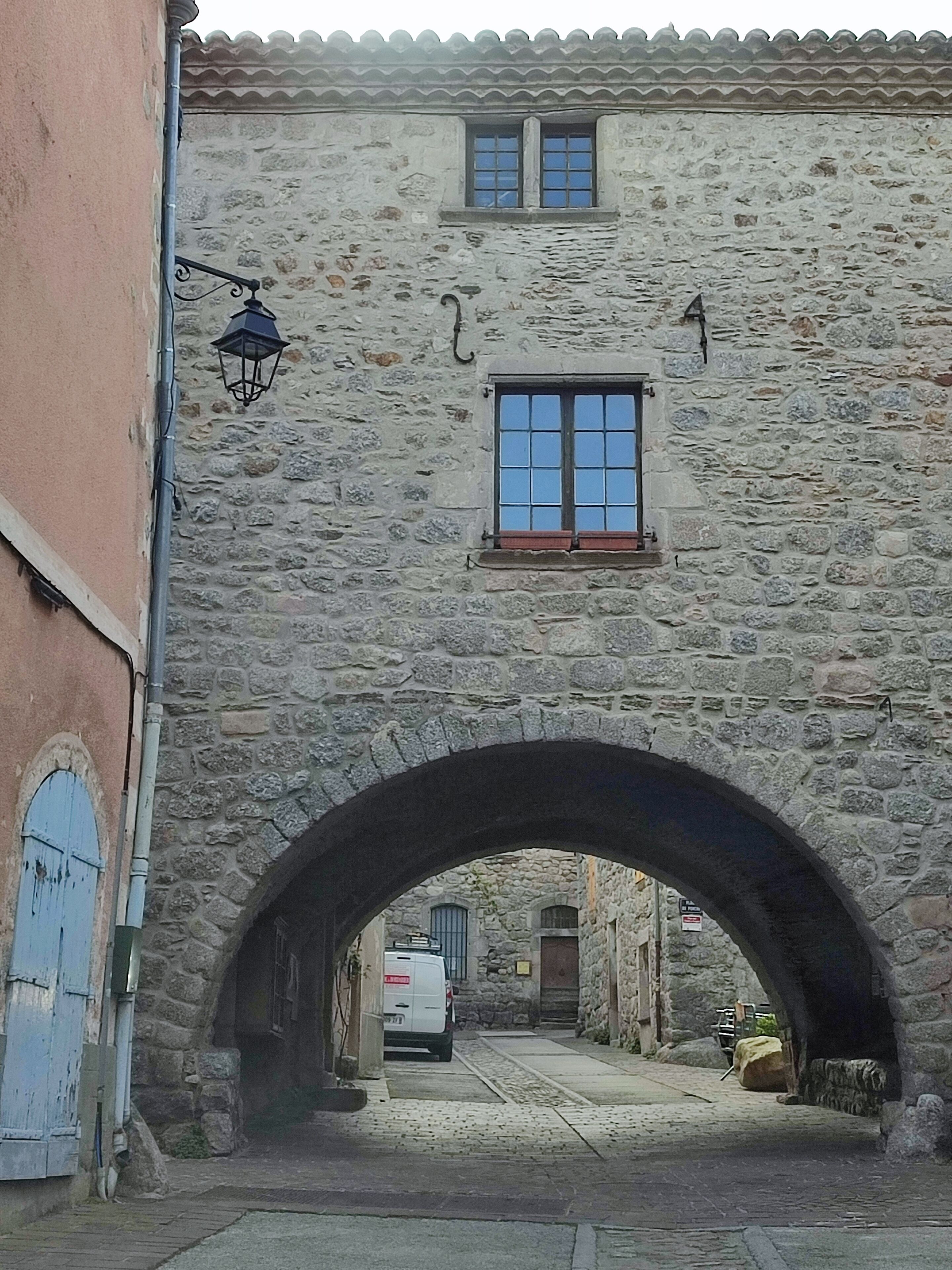 Ein Gebäude aus Stein mit einem großen Bogenportal, einem kleinen Fenster und Blick auf die Straße.
