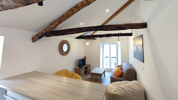 Un intérieur rustique avec des poutres apparentes, une table à manger en bois, un canapé et un téléviseur.
