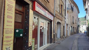 Une rue étroite, bordée de bâtiments des deux côtés, dont une boutique avec une enseigne indiquant « Boucheries » et une autre avec l’inscription « Capucine fleurs ».