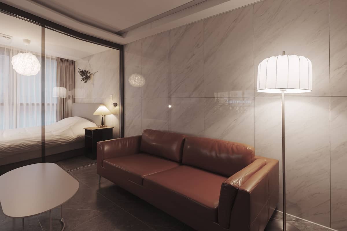 A modern hotel room with a bed, a leather sofa, a small table, and a floor lamp.
