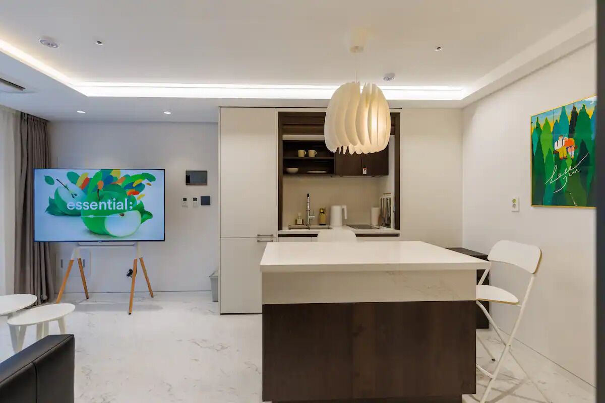 Et moderne køkken med en central ø, et fladskærms-TV og et spiseområde med stole.