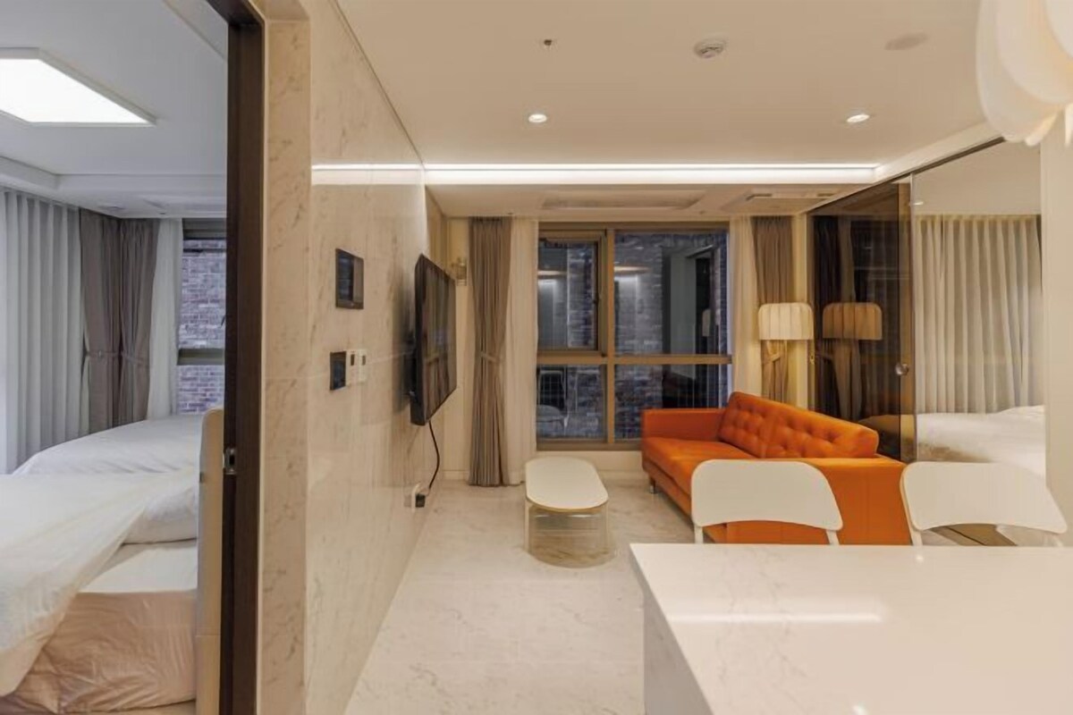 A modern hotel room with a bed, a sofa, a dining table, and a TV.