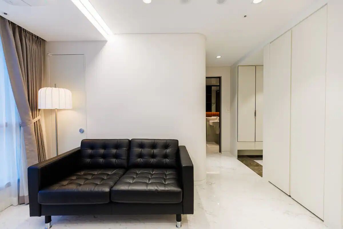 A modern living room with a black leather sofa, a floor lamp, and a white wall.
