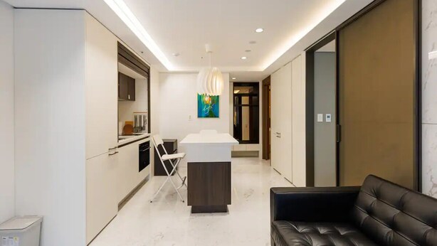 Una cocina moderna con una isla central, un comedor con mesa y sillas blancas, y un sofá de cuero negro.