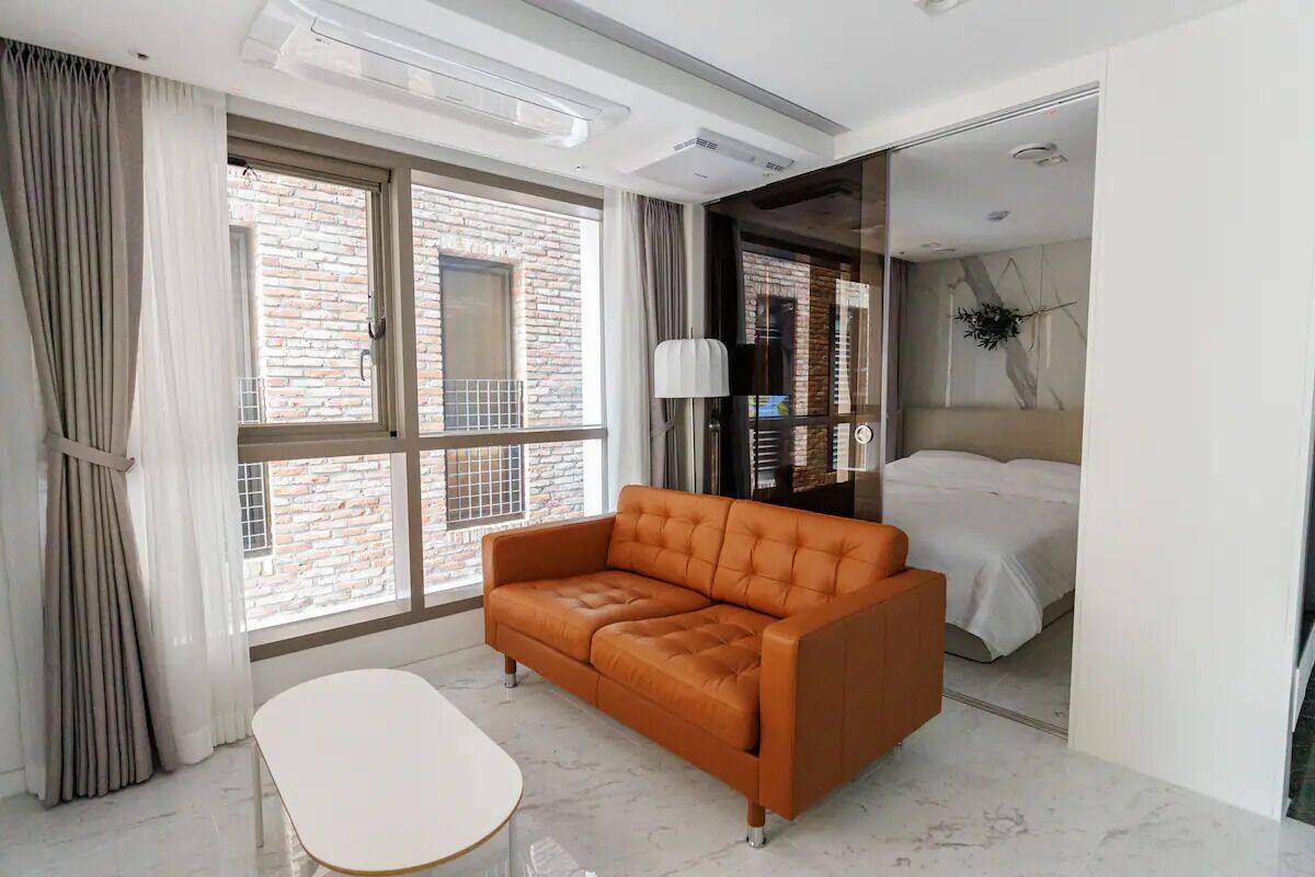 A modern hotel room with a large window, a sofa, a bed, and a small table.
