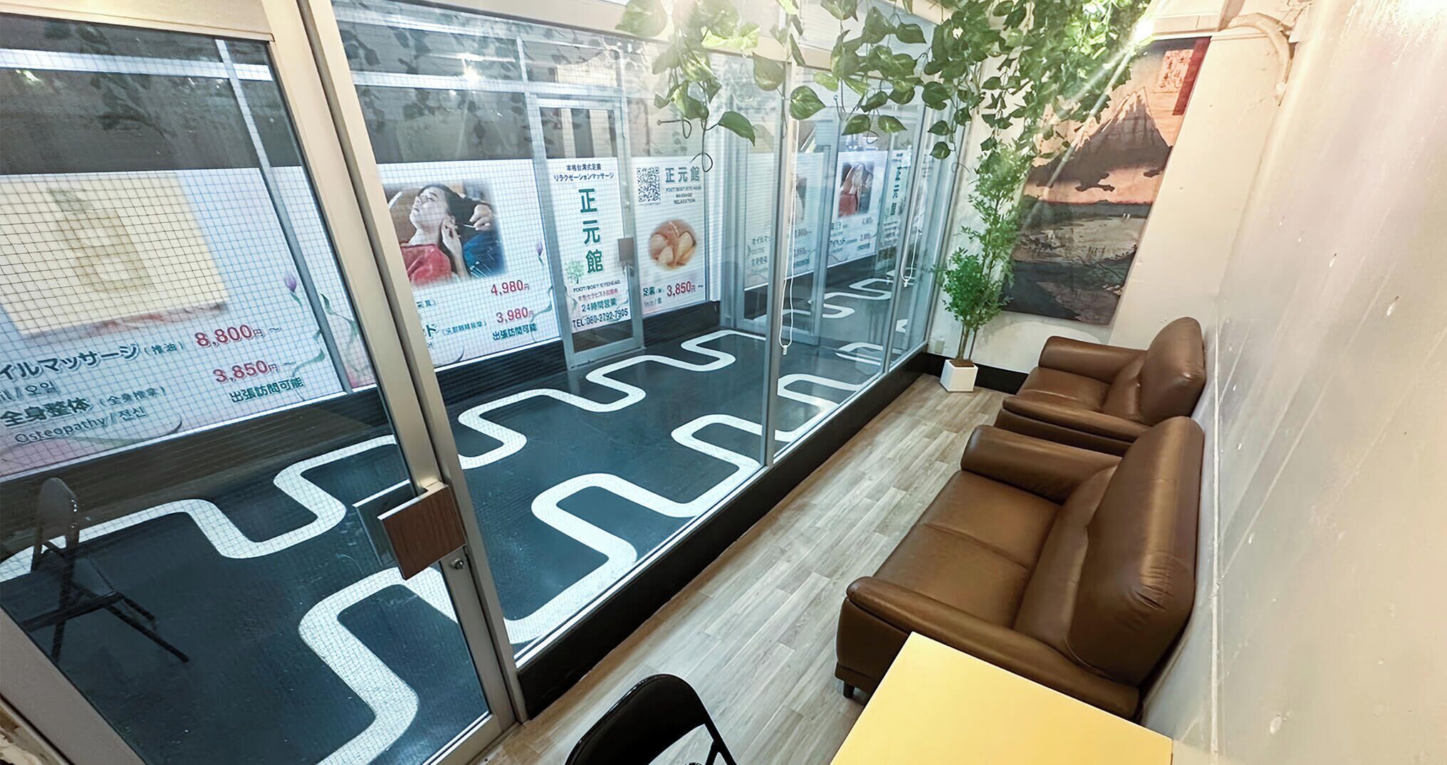 A modern interior with a seating area, a glass partition with advertisements, and a patterned floor.