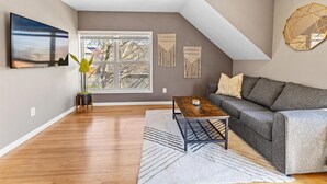 Un salon moderne avec un canapé gris, une table basse en bois, une grande fenêtre et un tableau accroché au mur.