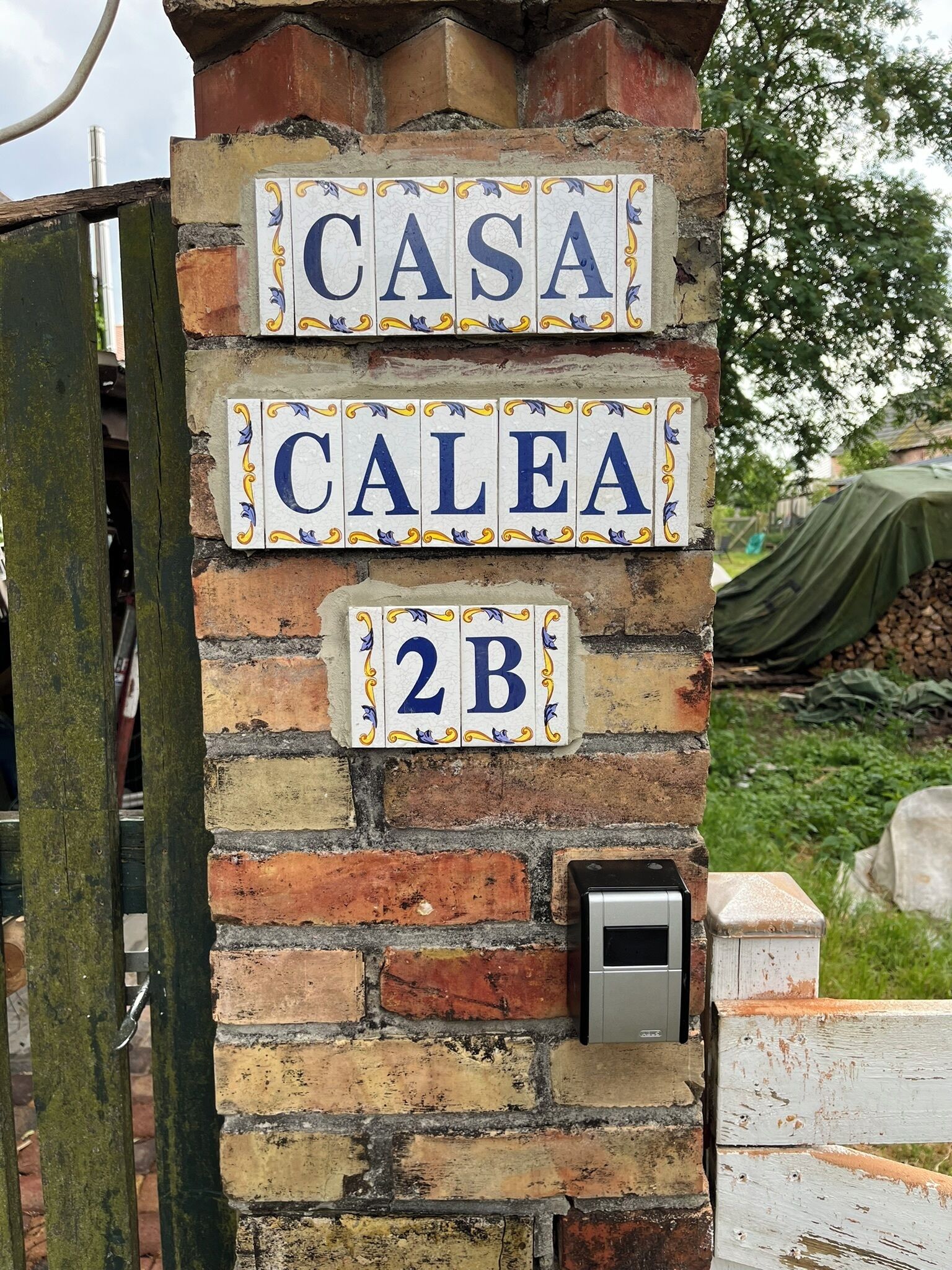 A brick wall with three ceramic house number signs: "CASA," "CALEA," and "2B."