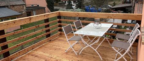 Una terraza de madera con una mesa y sillas de vidrio, rodeada por una barandilla de madera.