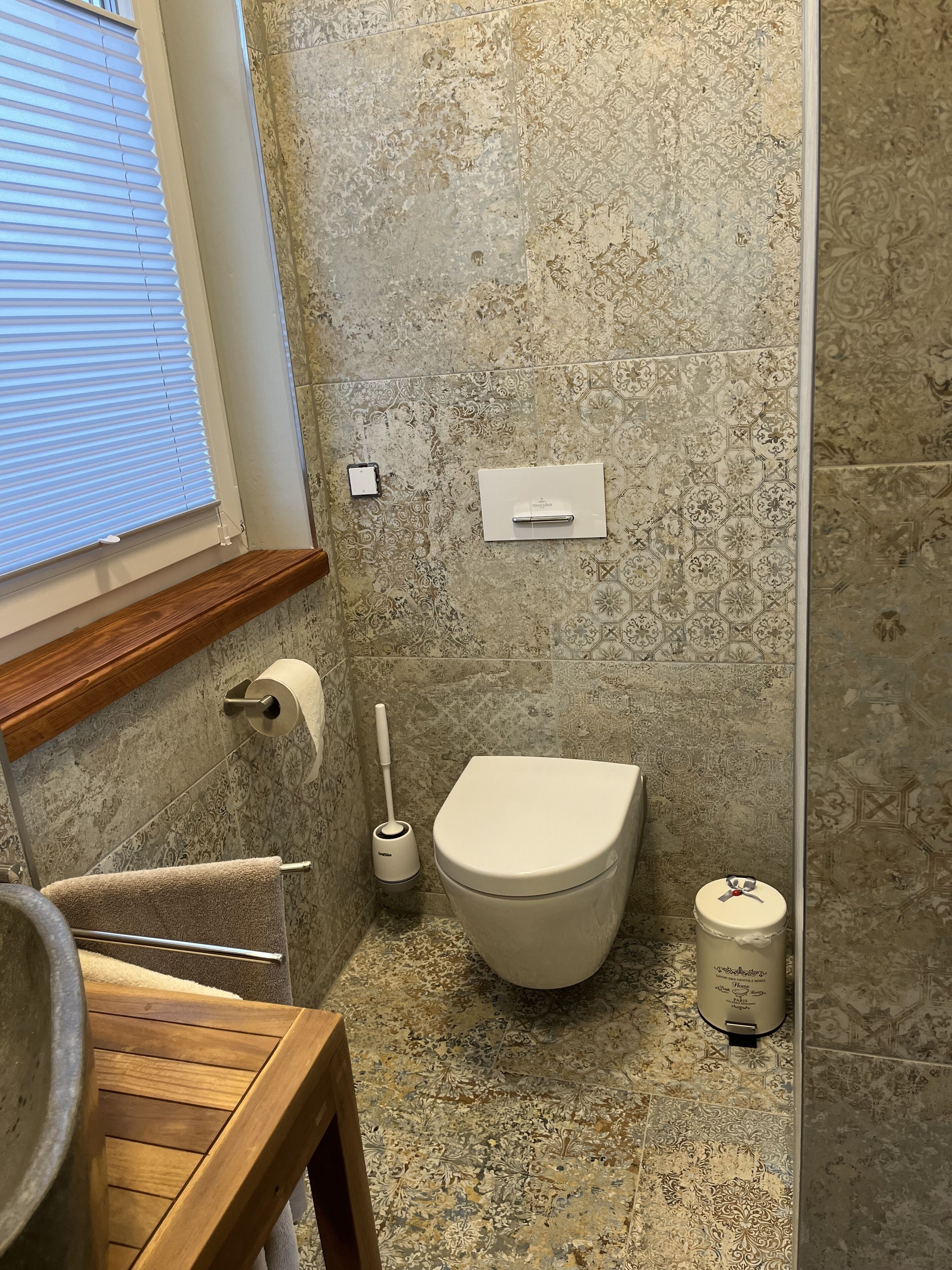 A bathroom with a toilet, a bidet, a towel rack, and a window with blinds.