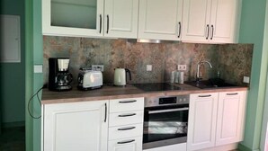 Una cocina con armarios blancos, encimera de granito, cafetera, tostadora y horno.