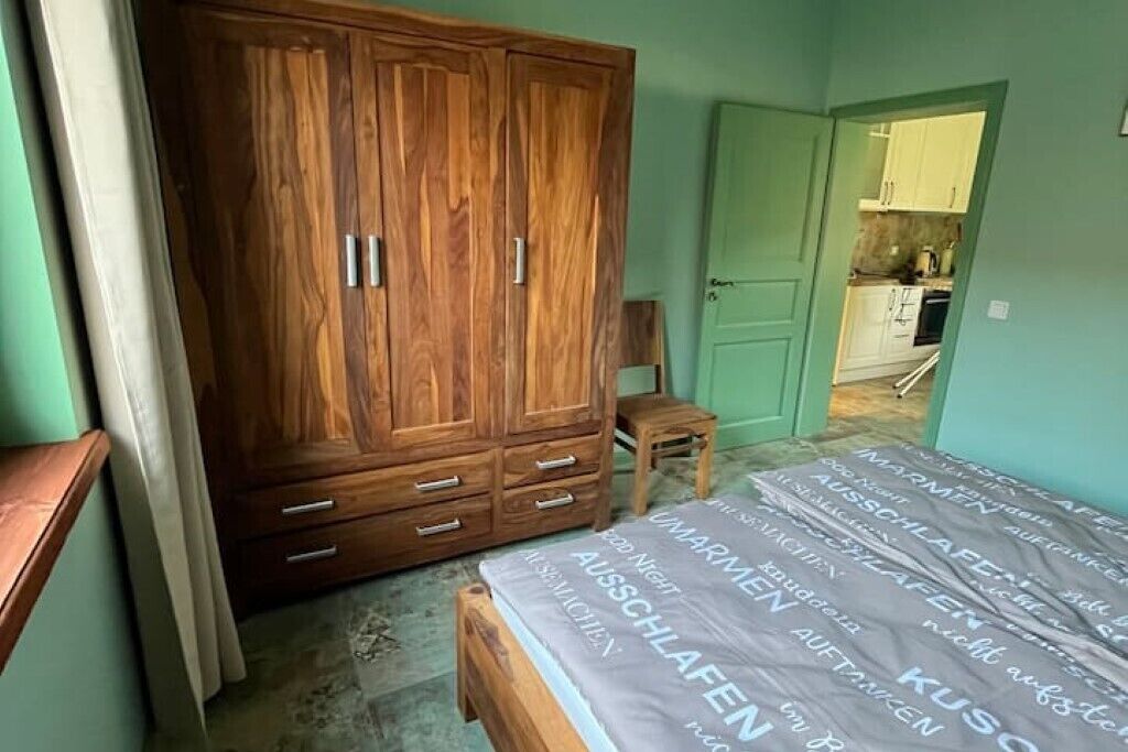 Ein Schlafzimmer mit einem Holzschrank, einem Bett mit gemustertem Überwurf und einem kleinen Holzschemel.