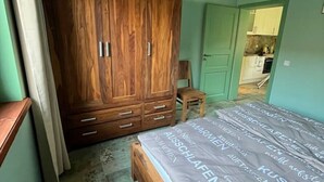 Un dormitorio con un armario de madera, una cama con colcha estampada y un taburete de madera.