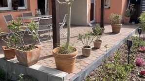 Un patio con mobiliario exterior, plantas en macetas y un edificio con balcón de madera.