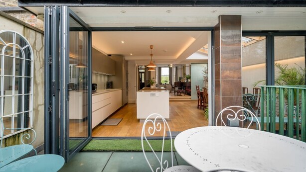 A modern kitchen with a central island, a dining area with a round table, and a patio with a green lawn. - Beautiful 6bed house near Kensinghton Park (London)