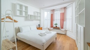 A modern bedroom with a large bed, built-in shelving, a radiator, and a window with curtains. - Beautiful 6bed house near Kensinghton Park (London)