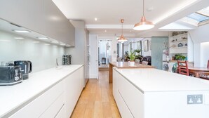 A modern kitchen with white cabinetry, a central island, pendant lighting, and a view into the dining area. - Beautiful 6bed house near Kensinghton Park (London)
