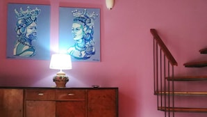 A room with a pink wall, a wooden cabinet with drawers, a lamp on the cabinet, and a staircase to the right.