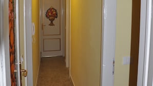 A narrow hallway with a carpeted floor, a door with a fruit decoration, and a hanging light fixture.