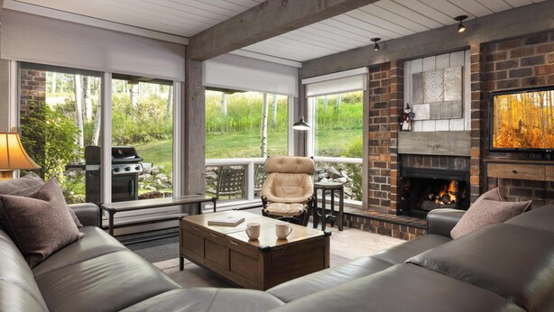 Un salon moderne avec une cheminée, des canapés en cuir, une table basse et de grandes fenêtres donnant sur un jardin.